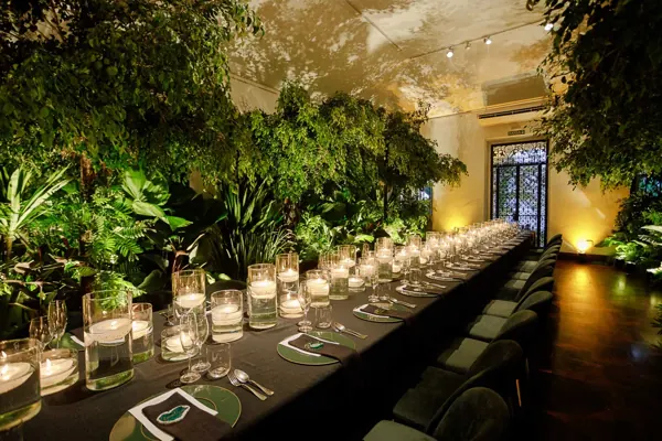 Long candlelit table surrounded by greenery at a corporate event